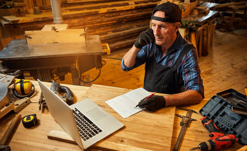 senior-carpenter-works-computer-talks-phone-with-client-workshop